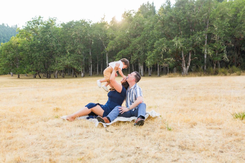 Family sitting in field playing with their little boy at Whistler's Bend Park for photos in Roseburg, Oregon. 